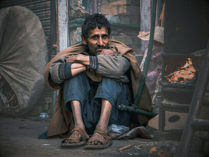 Warming oneself by the flame of a makeshift stove, the poignant image of a humanity relegated to the margins, forgotten by a system that replaces solidarity with indifference