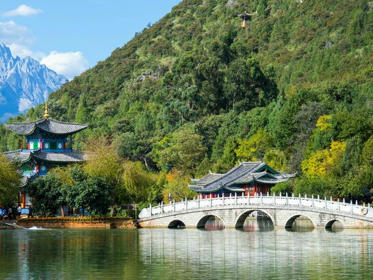 A historic stone bridge leading toward classical pavilions at Jade Dragon Snow Mountain, China, symbolizing the harmony between centuries-old traditions and contemporary development