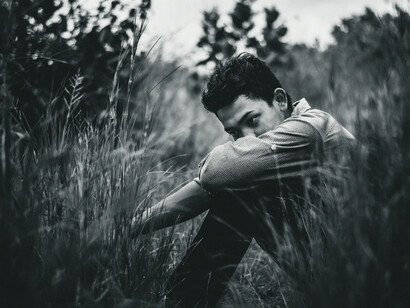 Joven sentado en el pastizal, mirando al suelo