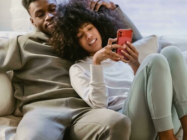 A joyful Black couple lounges on a couch, watching a vertical microdrama on a smartphone