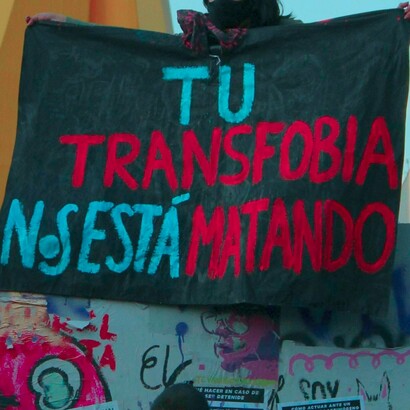 Bandera enarbolada durante una manifestación, que dice "Tu transfobia nos está matando"