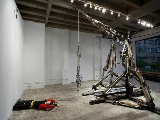 Andra Ursuta, Vandal Lust, 2011, Trebuchet: wood, plastic, cardboard, elastic rope, metal. Body: foam, plastic, fabric, leather, wax. 114 x 114 x 126 in. (365 x 365 x 320 cm), 9 x 60 x 50 in. (22 x 152 x 127 cm). Photo by Uli Holz. Courtesy of the artist and Ramiken Crucible, New York.