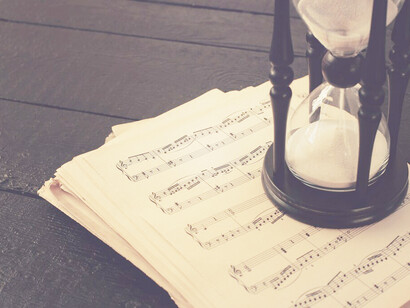 An hourglass sits beside sheets of paper adorned with music notes, symbolizing the passage of time through musical notation