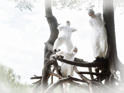 Three people stand in the trees, dressed in plastic suits, and wearing masks