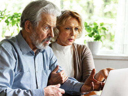 A distressed elderly couple looks shocked while reading fraudulent information on their computer at home
