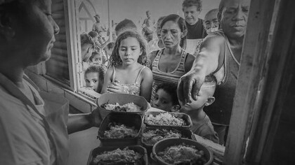 Fila de pessoas em programa social brasileiro. O mercado de trabalho mostra avanços insuficientes para sustentar crescimento. A informalidade continua elevada; os rendimentos têm progresso limitado; e parte significativa das vagas criadas oferece baixa estabilidade. Esse cenário é reflexo de um histórico de estagnação produtiva, que limita a criação de empregos qualificados e mantém grande parte dos trabalhadores em condições precárias. Para as famílias, o custo de vida se mantém alto, mesmo em períodos de inflação controlada. O preço de itens essenciais pressiona o orçamento doméstico e limita o consumo, criando sensação constante de aperto financeiro. Essa percepção pesa mais do que indicadores formais e alimenta frustração social