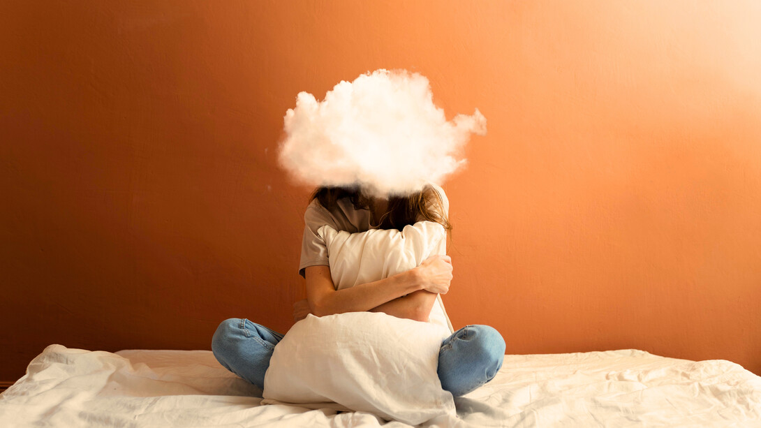 A woman sitting on her bed with a cloud in place of her head, representing the mental fog created by constant overthinking