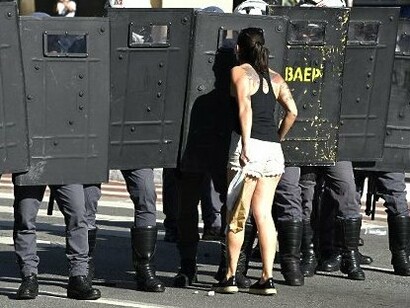 Uma manifestante aproxima-se de uma linha de policiais de choque durante um protesto. A cena ilustra as tensões que podem emergir no espaço público, um dos cenários em que se confrontam diferentes projetos de sociedade e de democracia