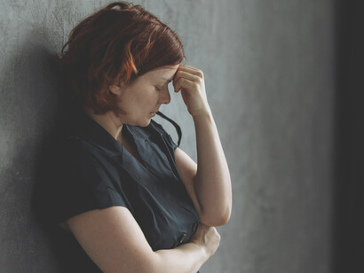 A stressed woman leans against a concrete wall, capturing a moment of emotional exhaustion and quiet depression