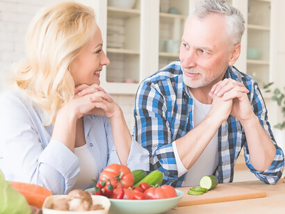 Capture a heartwarming moment in a modern kitchen as a senior man admires his wife cutting vegetables, promoting family bonding and healthy meal preparation as essential elements of a fulfilling lifestyle