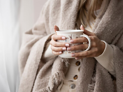 In the winter ambience, a woman, clad in snug attire, savors her coffee, indulging in the soothing warmth it brings