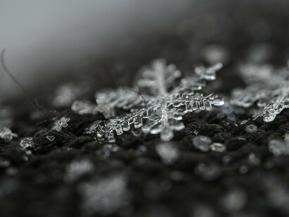 Highlighted against a dark, out-of-focus backdrop, a symmetrical snowflake reveals its delicate branches and hexagonal center, a quintessential symbol of winter's touch