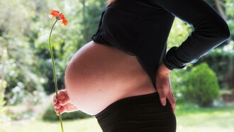 A pregnant woman in her final trimester holding the stem of a healthy flower anticipating her miracle