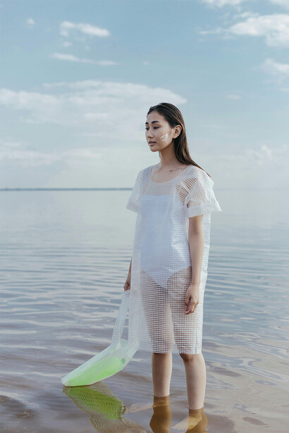 Modelo com roupa de plástico no mar. A busca por tinturas naturais e processos de tingimento sustentáveis reflete o comprometimento da indústria em reduzir o impacto químico no meio ambiente