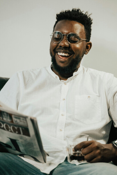 A man in a white long-sleeved shirt and eyeglasses reading a newspaper attentively
