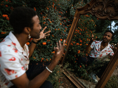 As the man looks at himself in the mirror, his hands up in the air