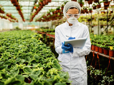 A female researcher studies the growth of flowers in a greenhouse, reflecting the progress of futuristic agriculture and cutting-edge biotechnology