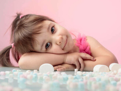A sweet young girl gazing at a table brimming with marshmallows, with a pastel pink backdrop