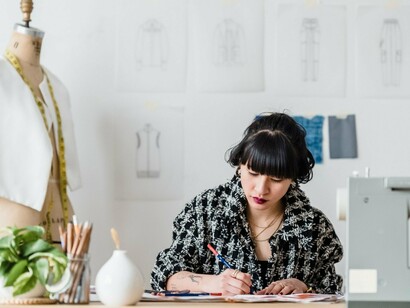 A fashion designer carefully sketching at her desk, representing the creative expertise and personal vision that remain at the heart of fashion design