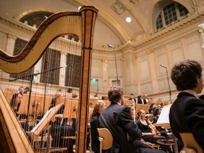 A choir performing under bright lights, accompanied by a solitary harp, at the Culture Casino Bern, in Bern, Switzerland