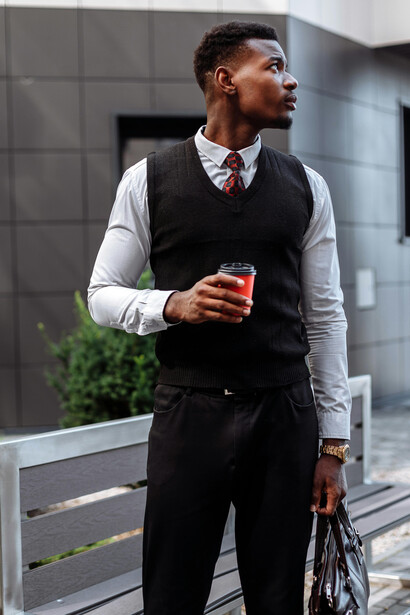 A professional in business casual attire stands holding a cup of coffee