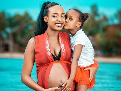A young girl kisses her pregnant mother on the cheek in a river in Africa