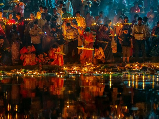 Devotees releasing glowing plates of offerings into the Ganges at night, reflecting a timeless act of faith and reverence