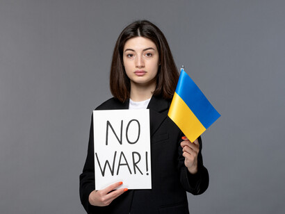 A young woman holding an Ukrainian flag and an anti-war sign