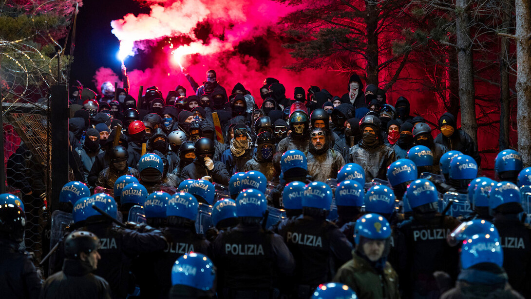 A heated standoff unfolds between riot police and protesters, the air thick with the anticipation of conflict and the weight of personal struggles behind every helmet