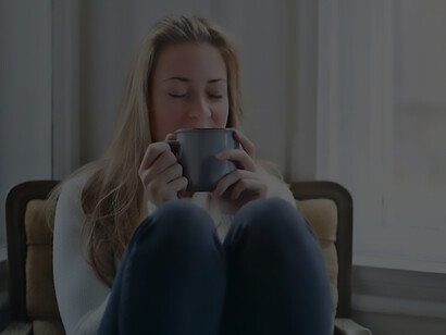 A picture of a woman, relaxed and sitting in an armchair next to a window, with the soft natural light streaming in