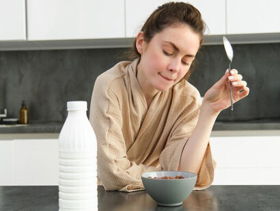 A girl baking in the kitchen, making dough while holding a recipe book, with milk and butter on the counter for cakes and cookies