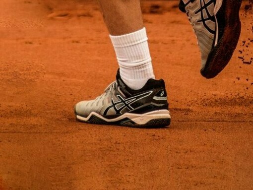 A low-angle shot of a player's legs and shoes in motion on a clay court