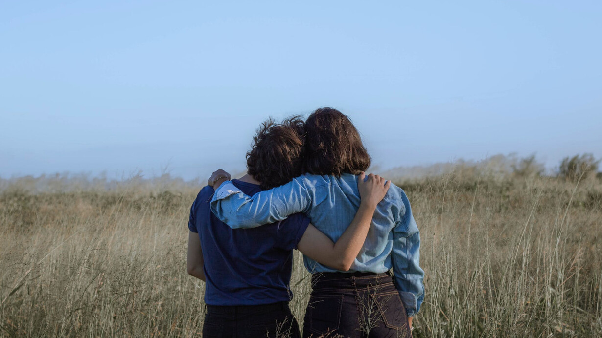 Due persone viste da dietro che si abbracciano in un campo di erba alta