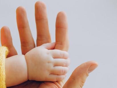 Bebê segura o dedo da mão do pai em gesto de conexão