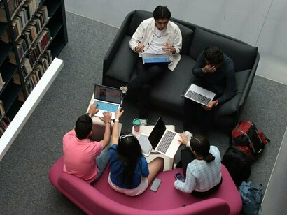 Students exchanging ideas with laptops and books around them, reflecting education as an investment in broader social productivity