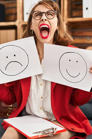 A young woman is holding papers with an unhappy face in one hand and a happy face in the other