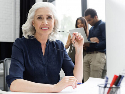 A smiling senior businesswoman sitting at her workplace, highlighting the presence and contributions of older adults in the workforce