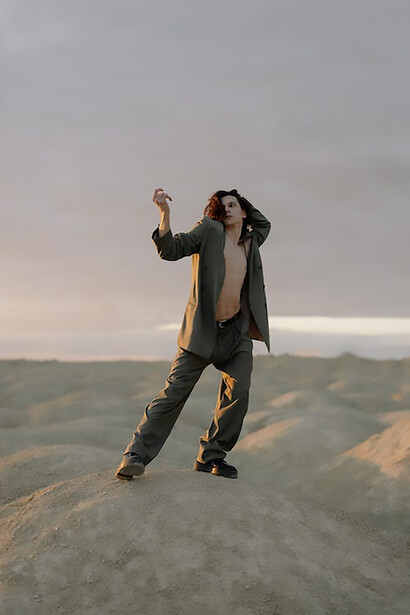 A man stands with grace on a weathered brown rock, clad in a refined ensemble of a sleek gray long-sleeve shirt and pants