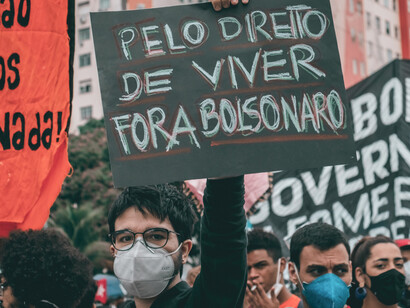 Un manifestante con mascarilla sostiene en alto una pancarta manuscrita en portugués que exige "Por el derecho a vivir/Fuera Bolsonaro" en medio de una manifestación popular