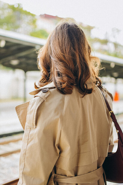 A woman waits on the platform at a train station, lost in thought as trains pass by