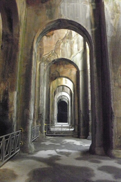 L'ambiente sotterraneo della cisterna, con la sua illuminazione naturale filtrata dalle aperture superiori, crea un gioco di luci e ombre che ha affascinato artisti e visitatori per secoli. RaBoe/Wikipedia. Bacoli (NA), Italia