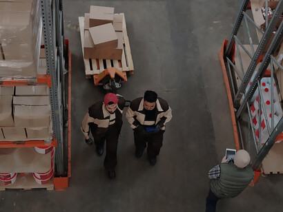 Within the expansive confines of a warehouse, a team of men collaboratively operates a pallet truck, skillfully transporting goods with synchronized precision