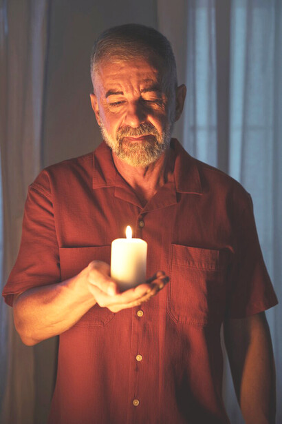 A man deeply engaged in prayer, with a candle in hand, reflecting the transformative power of redemption and renewal in his faith journey