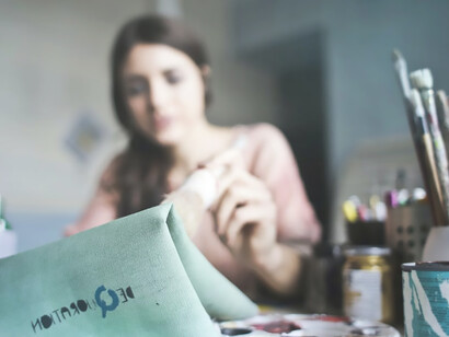 A woman sits at a table adorned with a myriad of paintbrushes, immersed in the act of painting