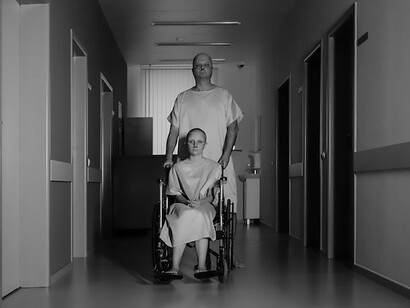 Quietly positioned in a wheelchair, a patient observes the hospital corridor, their demeanor reflecting a blend of determination and quiet contemplation amid the bustling medical environment