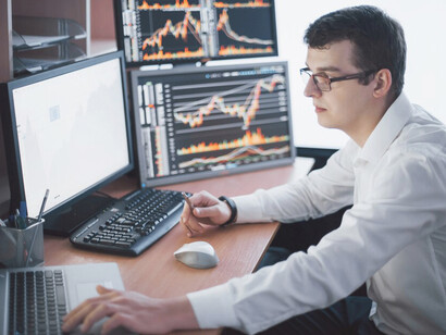A stockbroker in a shirt analyzes market data on display screens in a trading room, closely monitoring US stock market trends, forex, and economic instability amid growing financial risks