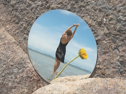 On a summer day at the beach, a woman elegantly poses, capturing the essence of the season, while a round mirror reflects her image, adding a touch of artistic allure to the scene