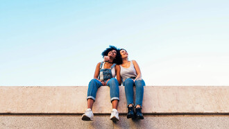Dos amigas observan el cielo sentadas en un muro