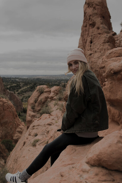 In a serene display of feminine consciousness, a woman finds solace and introspection as she sits on the rocks, nestled within the gentle embrace of the hills, symbolizing her harmonious connection with the rhythms of nature and her inner self