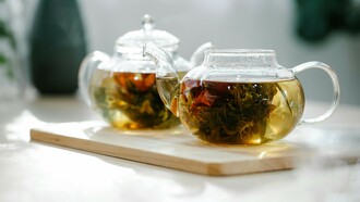 Two glass teapots filled with blooming tea flowers on a light wooden tray
